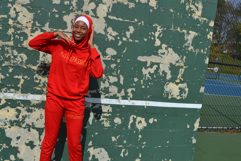 Woman smiling in the currant red jogging suit with the hood up, against a green wall