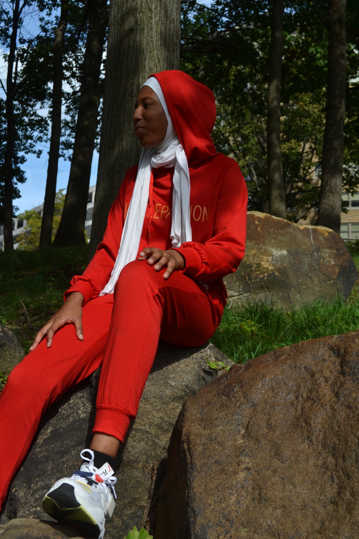 Woman in the currant red jogging suit with the hood up, sitting on rocks outdoors