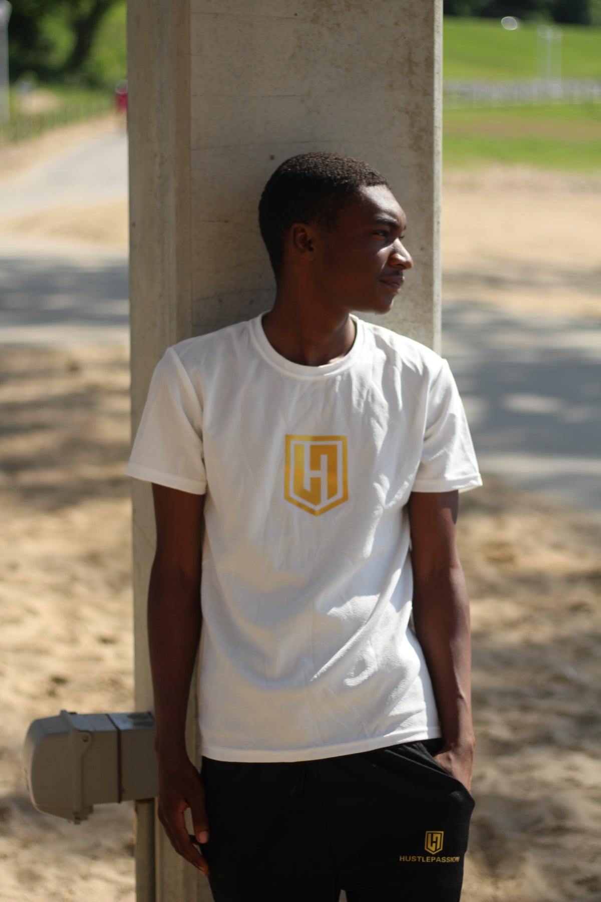 Model in a white Hustle Passion T-shirt and black shorts leaning against a concrete column