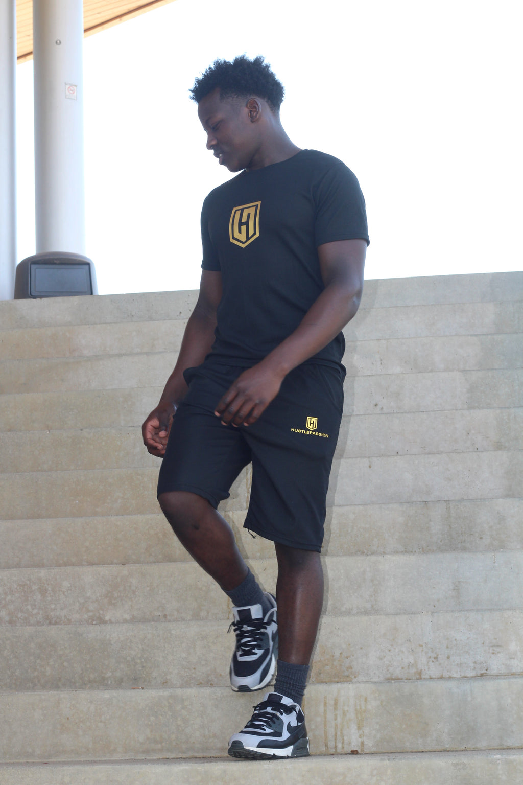 Model wearing the black Hustle Passion T-shirt and shorts set on concrete steps
