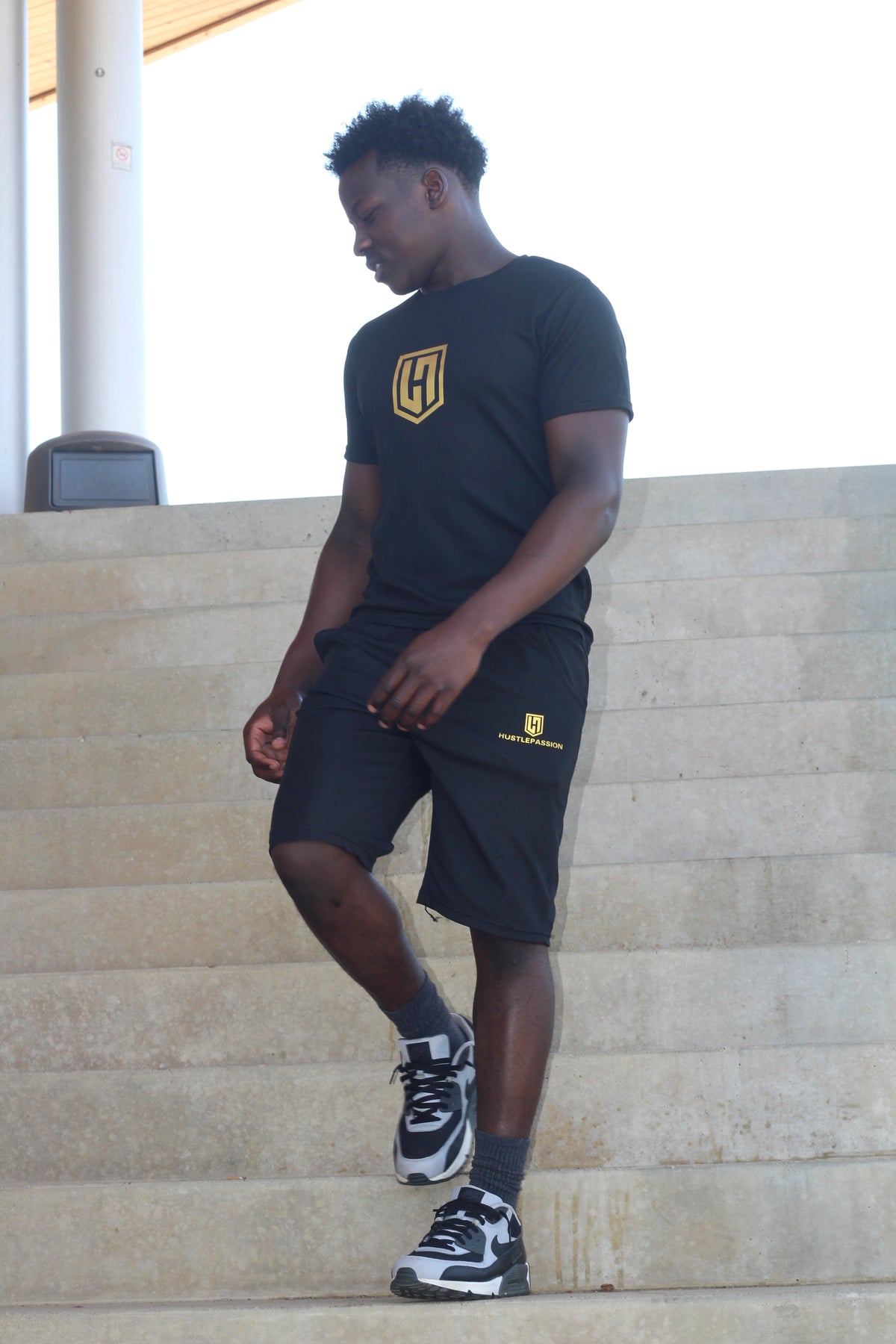 Model wearing the black Hustle Passion T-shirt and shorts set on concrete steps