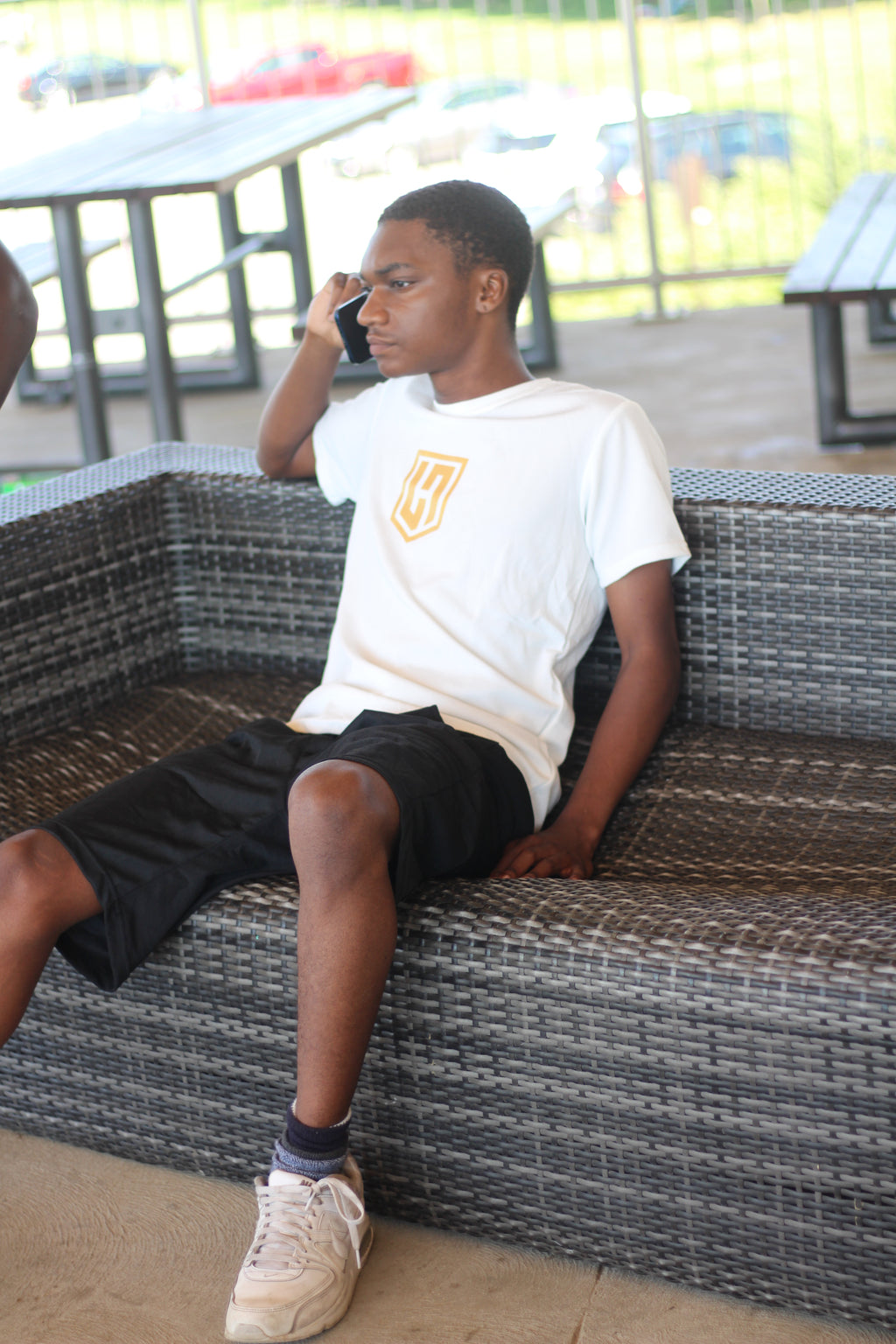 Model in a white Hustle Passion T-shirt and black shorts, sitting on an outdoor sofa