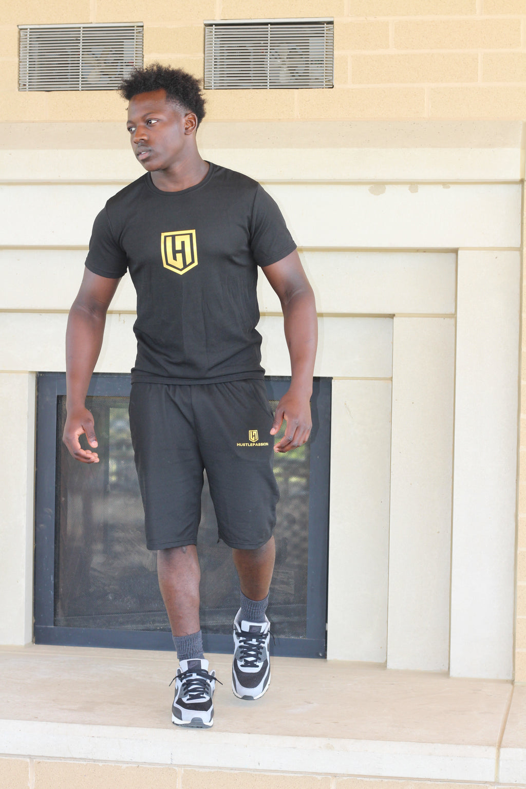 Model wearing the black Hustle Passion T-shirt and shorts set, standing on front steps