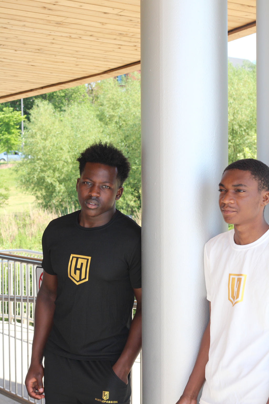 Two models in Hustle Passion tee and shorts outfits standing by a column outdoors