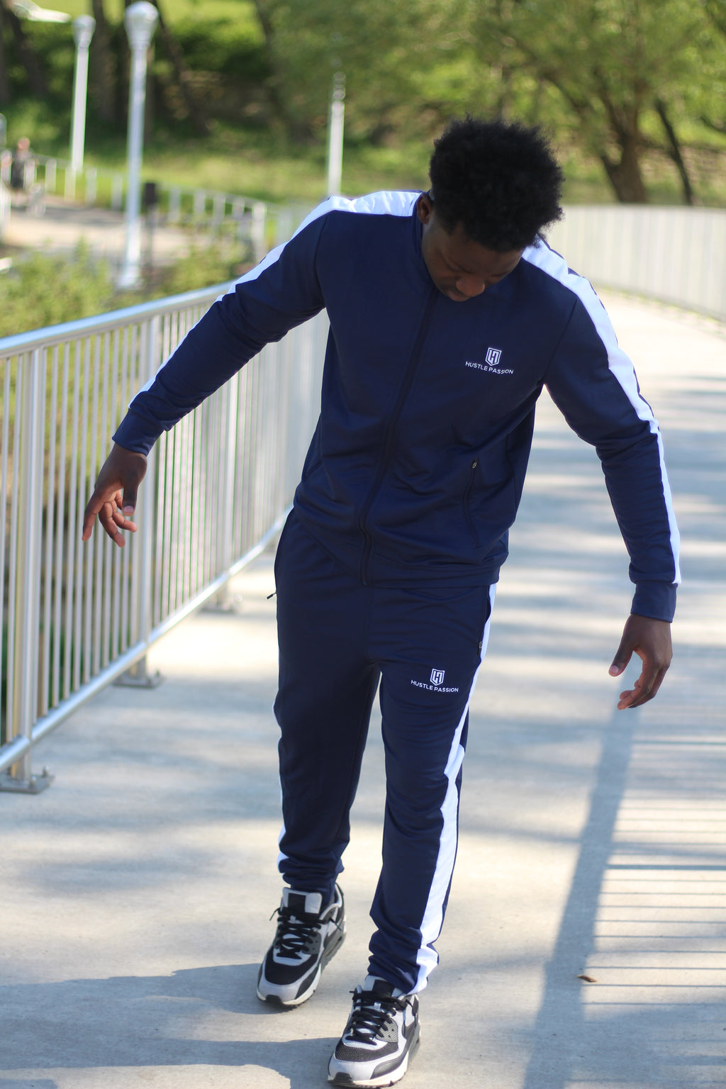 Model in the navy blue tracksuit with white side stripes walking on a paved path