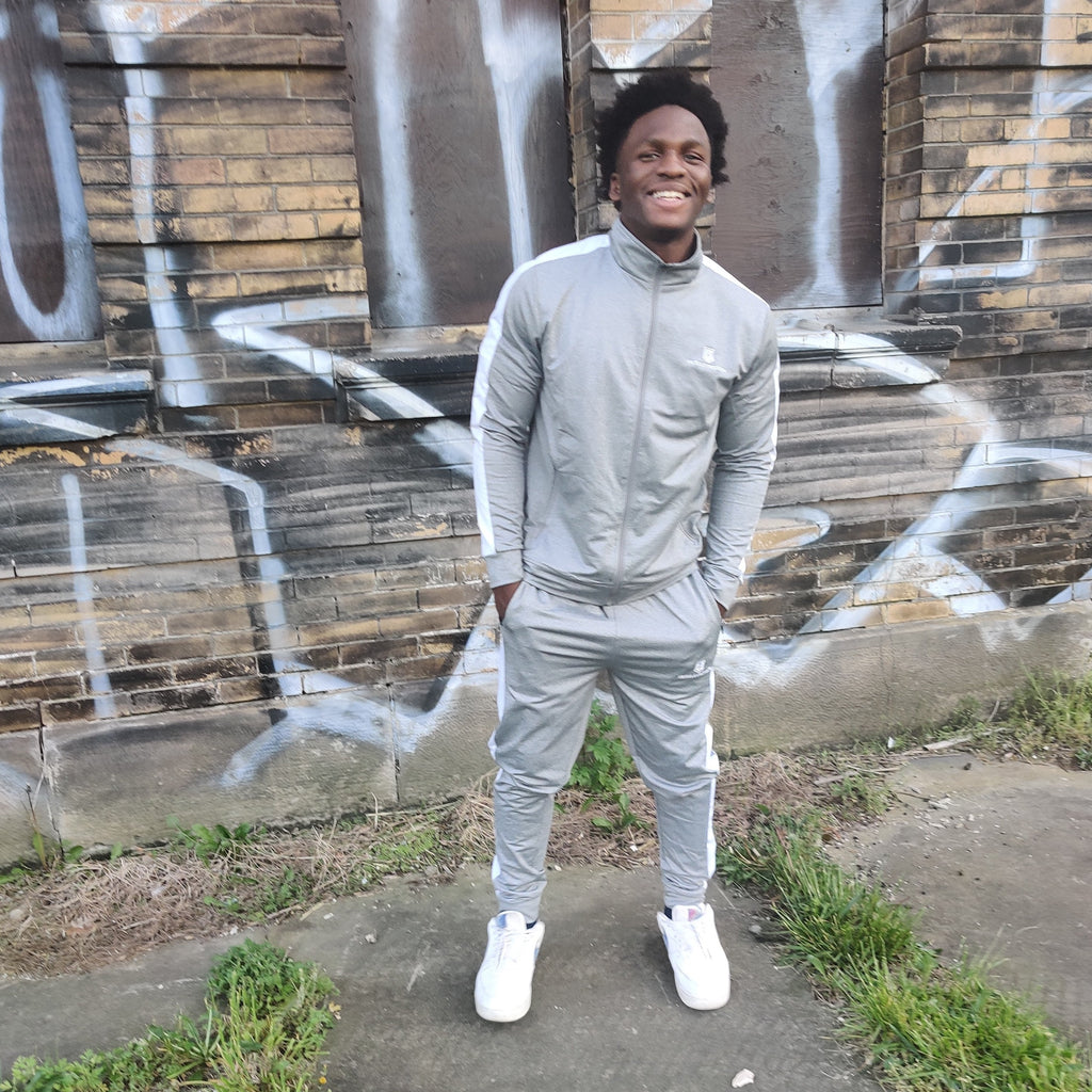 Model wearing the Hustle Passion light grey tracksuit set, standing in front of a graffiti wall