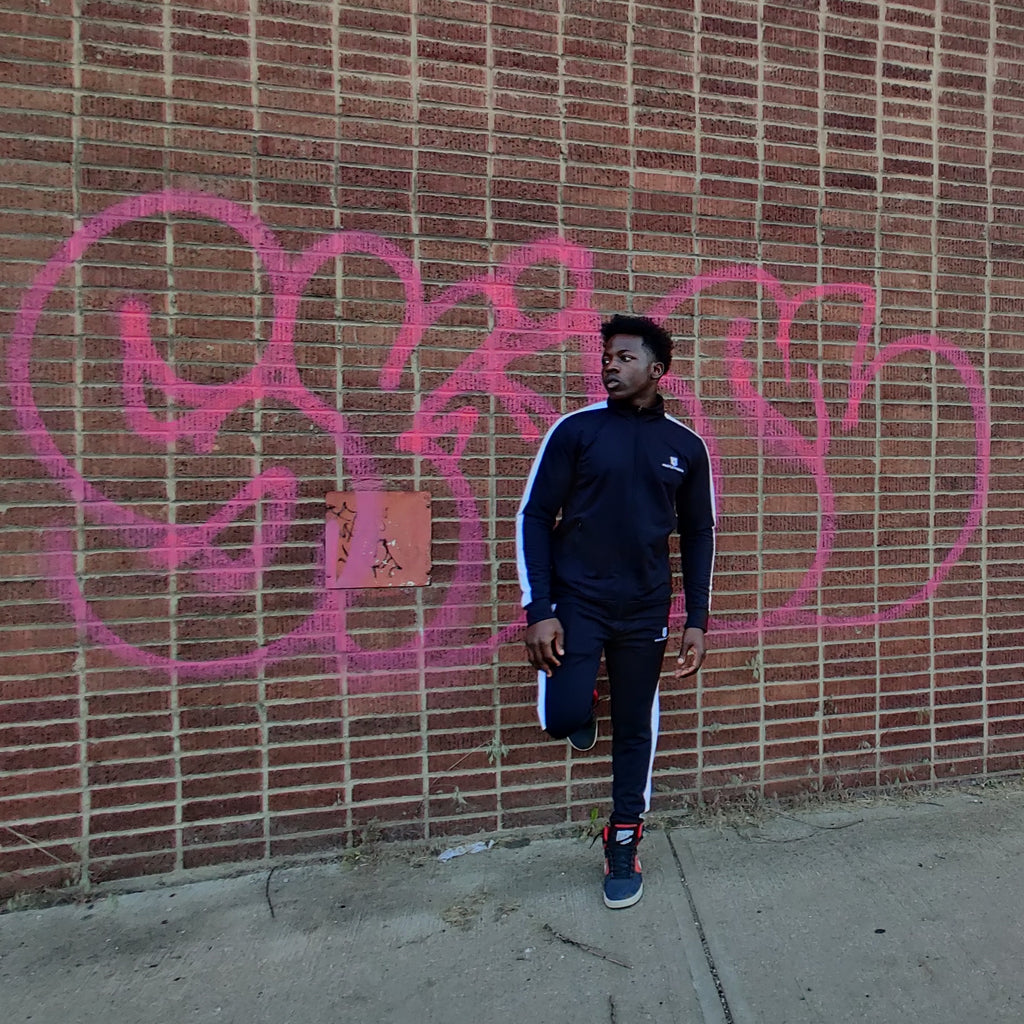 Model in the pitch black tracksuit standing against a brick wall with pink graffiti