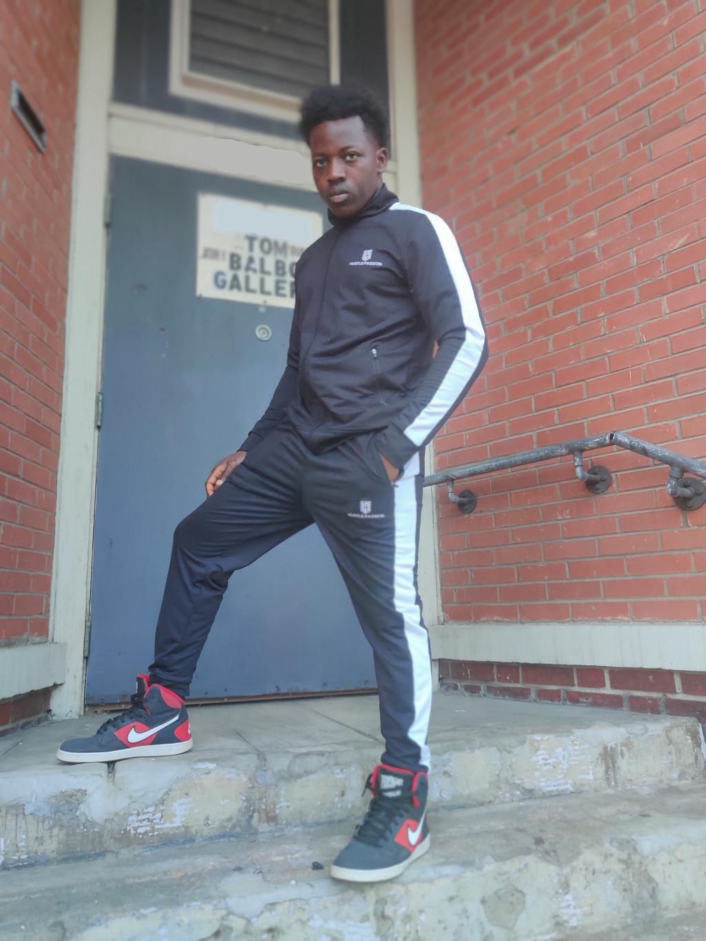 Model standing on steps wearing the pitch black tracksuit with white side stripes